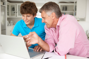 A father teaching his 16 year old son how to manage his teenage savings account online.
